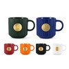 A ceramic mug set in green, navy, red, orange, black, and white, each featuring a bronze medal design on the front.