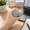 A grey stress ball with a bumpy texture held in a hand, placed on a desk with a laptop and a plant nearby.