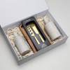 A gift box containing two cream bottles and a wooden cheese knife set, arranged on shredded paper.