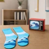 A retro TV-style gift box in red with a pair of blue and white wave-patterned socks beside it on a wooden surface.