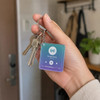 A person holding a translucent purple and blue acrylic keychain featuring a music play button and a keyring.