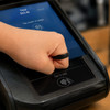 A hand wearing a black NFC carbon fibre ring is tapping a payment terminal screen.