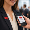 A woman in a suit with a red pin badge, while a hand holds a phone near the badge to connect.