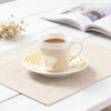 A ceramic coffee mug in white with yellow patterns, filled with coffee, resting on a matching saucer.