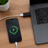 A black USB data blocker connects a smartphone to a laptop, displaying a charging graphic on the phone.