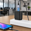 A black USB data blocker with a blue and silver connector, plugged into a power strip beside a smartphone.