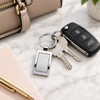 A silver frame keytag attached to keys and a car remote, resting on a marble surface beside a pen and planner.