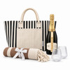 A striped tote bag, a bottle of sparkling wine, two glasses, and a rolled blanket with a ribbon.