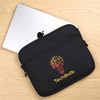 A black laptop sleeve featuring a logo design, with a silver laptop partially visible behind it on a wooden surface.