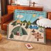 A tapestry blanket featuring a camping scene with mountains, trees, a tent, and a caravan in green and blue hues.