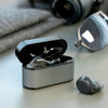 Wireless earbuds in a grey charging case, with one earbud outside the case, set on a flat surface.