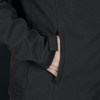 A black softshell jacket featuring a zipped pocket and a smooth fabric texture. It has a logo on the surface.