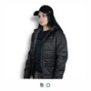 A black Swiss Peak Urban Puffer Jacket worn by a woman, paired with a black cap. The jacket features a logo.