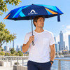 A man holding a large blue umbrella with geometric designs and a logo, standing by a waterfront city view.