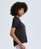 A black short-sleeve tee, featuring a relaxed fit and subtle branding. The model poses with a natural curly hairstyle.