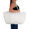 A large white reusable grocery bag with long handles, held by a person standing sideways.