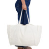 A large, white reusable grocery bag with two handles, held by a person in blue jeans.