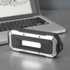 A rugged black and silver waterproof Bluetooth speaker placed beside a laptop on a metallic surface.