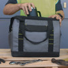 A grey and black cooler bag with a side mesh pocket and a logo, being filled with a drink bottle.