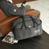 A grey duffel bag with multiple pockets and a logo, resting on a table next to a person sitting on a couch.