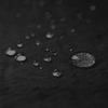 A close-up of water droplets on a textured black surface, showcasing various sizes and reflections.
