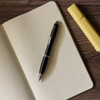 A black plastic pen lies on a blank notebook alongside a yellow highlighter.