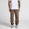Brown track pants with a relaxed fit, featuring tapered legs and elastic cuffs. The model wears a plain white t-shirt.