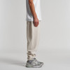 A pair of cream track pants with a relaxed fit, featuring a side pocket and worn with grey sneakers.