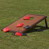 A Backyard Cornhole Set featuring a wooden board and red and black bean bags, placed on grass.