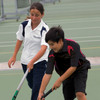 A white polo shirt with navy accents and a dark polo shirt with red accents, worn by two young athletes on a tennis court.