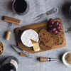 A wooden cheese board with brie cheese, crackers, grapes, and cheese knives, accompanied by a bottle of wine.