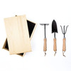 A wooden box with a black interior, alongside three garden tools with wooden handles: a trowel, cultivator, and hand rake.
