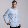 A light blue button-up shirt for men, featuring a collar and a chest pocket, with a logo on the fabric.