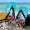 Bright blue flip flops featuring a flamingo design and black straps, placed on sandy beach with a straw hat.
