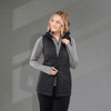 A black insulated puffer vest with a zip front, worn over a grey long-sleeve top, featuring a logo.
