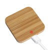 A square bamboo wireless charger in a natural wood finish with a white charging cable connected.