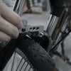 A multi-tool in metallic grey being used on a bike's fork and wheel, featuring a black tyre with a textured pattern.
