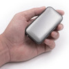 A compact silver wireless speaker held in a hand, featuring a perforated design and a sleek shape.