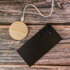 A round bamboo wireless charger in natural wood colour next to a black smartphone on a rustic wooden surface.
