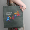 A person holding a grey tote bag featuring a colourful music-themed graphic and a branding logo.