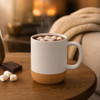 A white ceramic mug with a cork base, filled with hot chocolate and marshmallows, on a wooden table.
