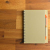 A Savannah Notebook featuring a spiral binding and a Matador Pen in orange, placed on a wooden surface.