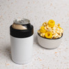 A drink bottle in white and black beside a bowl of popcorn topped with yellow candies. The bottle has a logo.