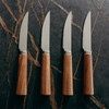 A steak knife set featuring four stainless steel knives with brown wooden handles, arranged on a dark stone surface.