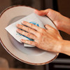 A dish cloth in grey and white is being used to wipe a plate in a kitchen setting.