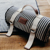 A rolled picnic blanket in navy and white stripes, with a leather handle and logo.