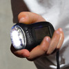 A black Dynamo Solar Torch held in a hand, featuring a bright light and a small display screen.