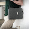 A grey laptop sling bag with a handle and adjustable strap worn by a person. The bag features a logo.