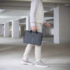 A laptop case in dark grey, being carried by a person in light-coloured pants, set in an industrial space.