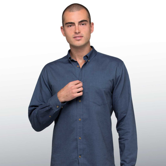 A man models a blue button-up shirt with a collar and a single chest pocket, featuring a logo on the shirt.